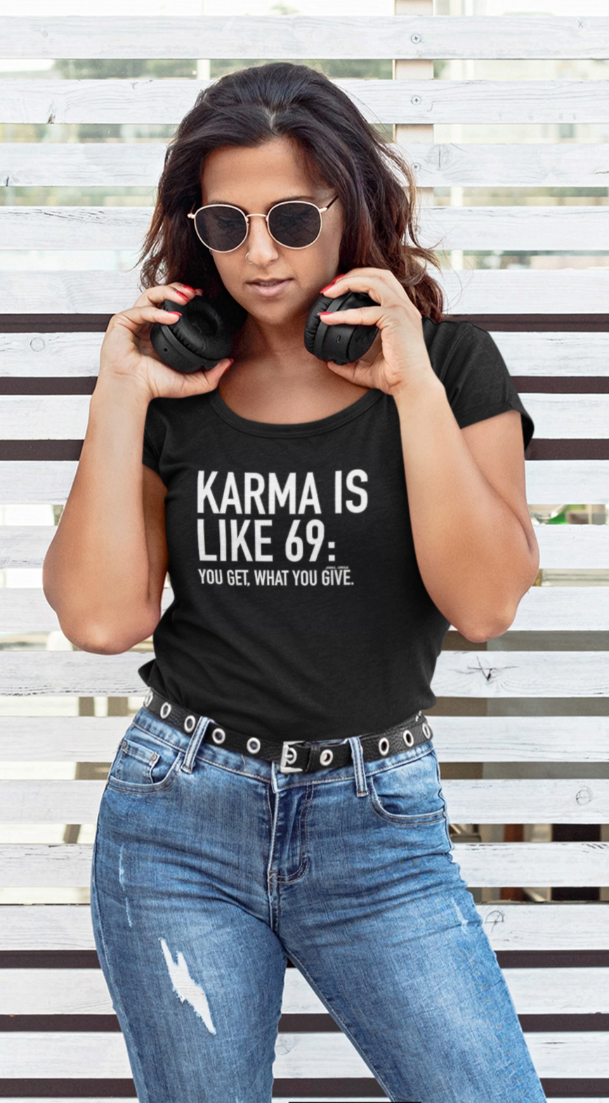 Woman wearing a black t-shirt with 'Karma is like 69: You get what you give' text, standing against a striped background.